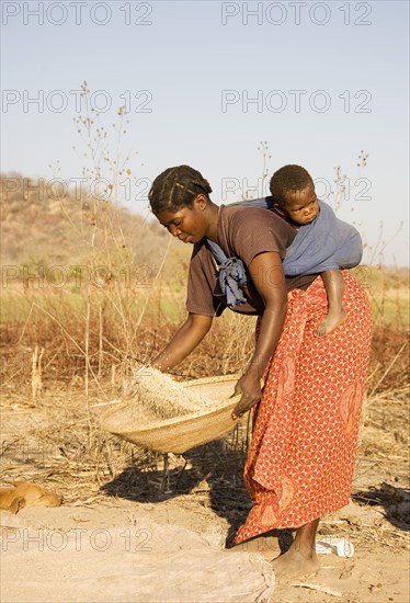 Tonga woman with child on her back sifting grains