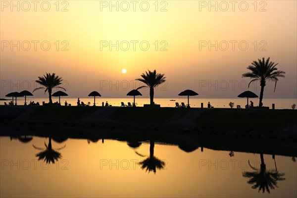 Sunset with water reflection from palm trees and sunshades