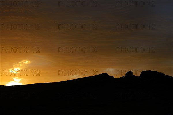 Dramatic sunset with rising storm clouds in front of mountain silhouette