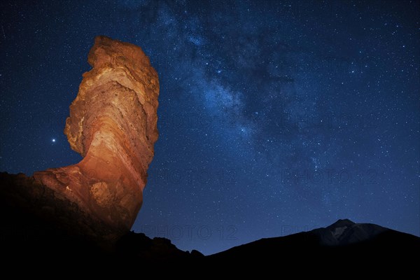 Illuminated Roque Cinchado in front of Pico del Teide with starry sky