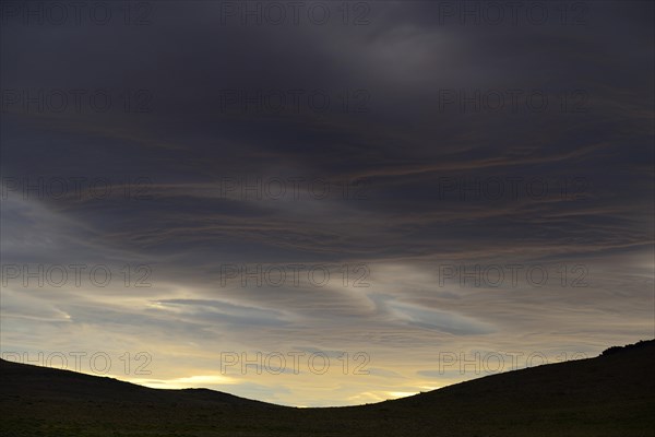 Dramatic sunset with rising storm clouds in front of mountain silhouette