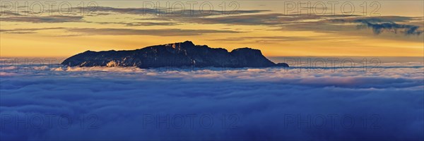 From the clouds towering mountain massif Hochthron at sunset