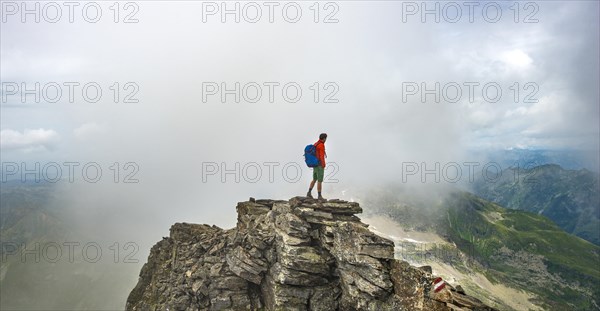 Hiker on the summit of the Hochgolling with rising fog