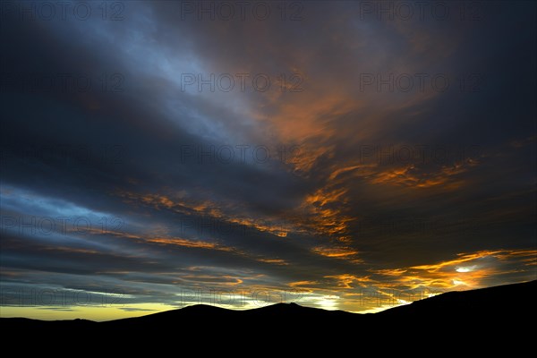 Dramatic sunset with rising storm clouds in front of mountain silhouette