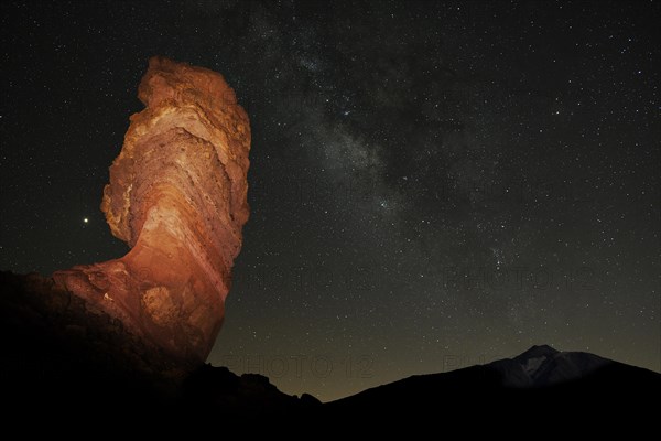 Illuminated Roque Cinchado in front of Pico del Teide with starry sky