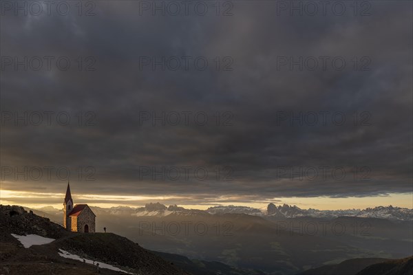 Latzfonser cross chapel at sunrise with dramatic clouds and South Tyrolean mountains