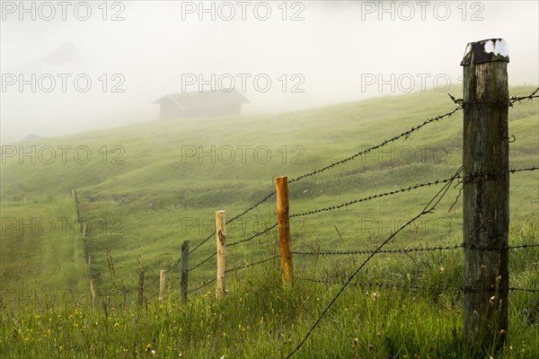 Pasture fence on mountain meadow with small cabin in the fog