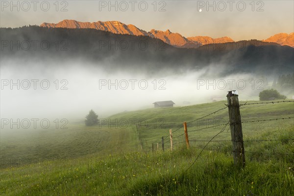 Pasture fence on mountain meadow with small cabin in the fog