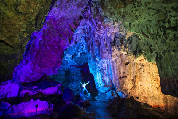 Young man in a colourfully illuminated stalactite cave