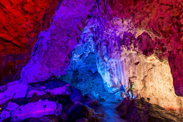 Man in a colourfully illuminated stalactite cave with stalagmites and stalactites