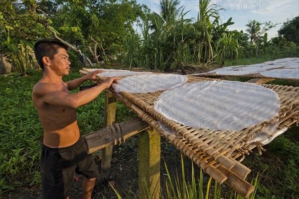 Vietnamese worker spreads steaming rice noodle patties on bamboo frame to dry