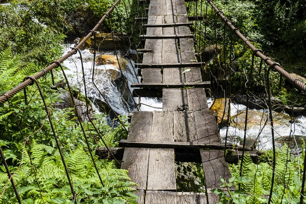 Old wooden suspension bridge across small river in Upper Modi Khola valley