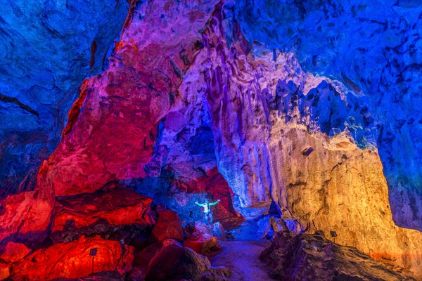 Man in a colourfully illuminated stalactite cave with stalagmites and stalactites