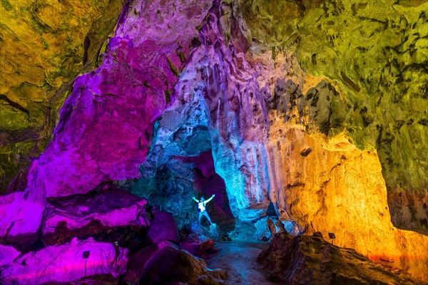 Man in a colourfully illuminated stalactite cave with stalagmites and stalactites
