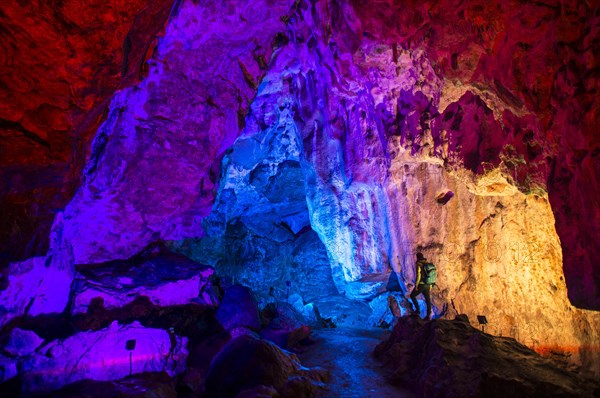 Young man looks at colorfully illuminated stalactite cave
