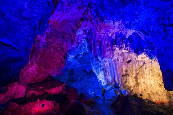 Young man looks at colorfully illuminated stalactite cave