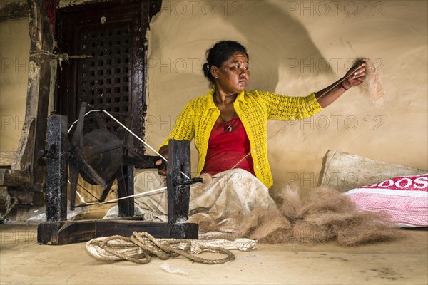 Native woman spinning sheep's wool with traditional spinning wheel in front of house