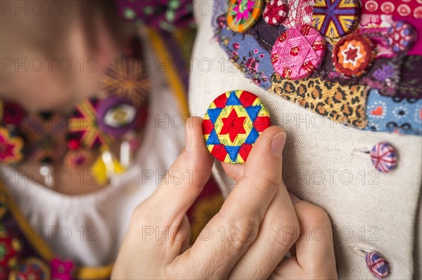 Button maker's hand fits the finished Posamentenknopf to Dirndl on a doll