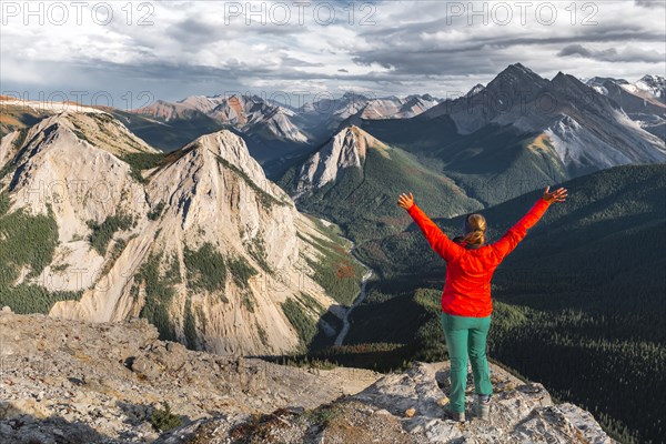 Female hiker with raised arms looking from summit over mountain landscape