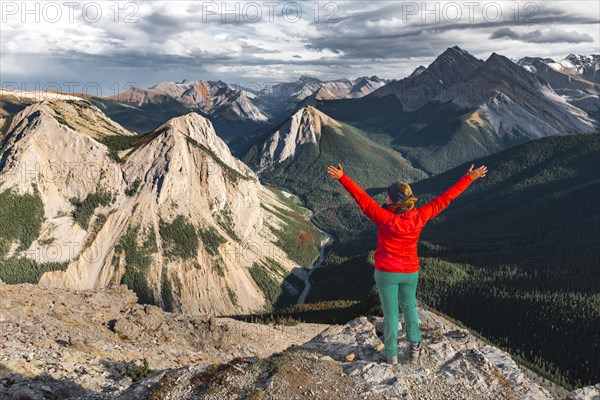 Female hiker with raised arms looking from summit over mountain landscape