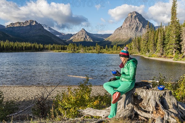 Young woman with breakfast at the mountain lake Two Medicine Lake in mountain landscape