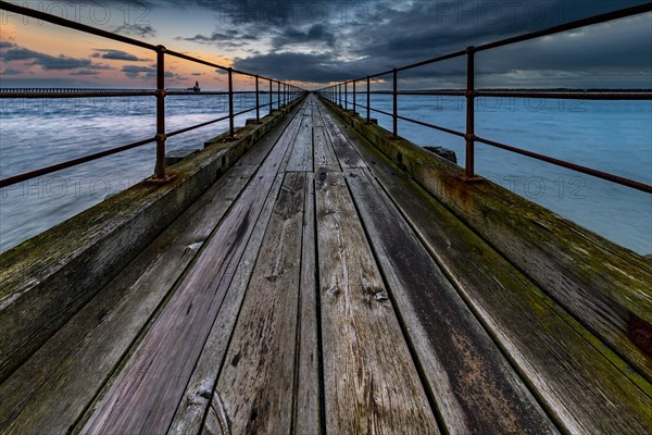 Old wooden jetty in the sea with dramatic clouds at sunset