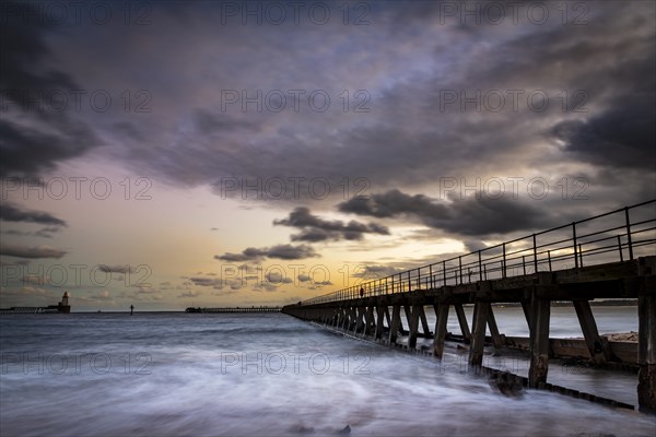 Bridge in the sea with dramatic clouds at sunset