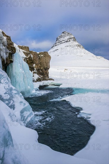 Frozen waterfall Kirkjufellsfoss and the mountain Kirkjufell with snow