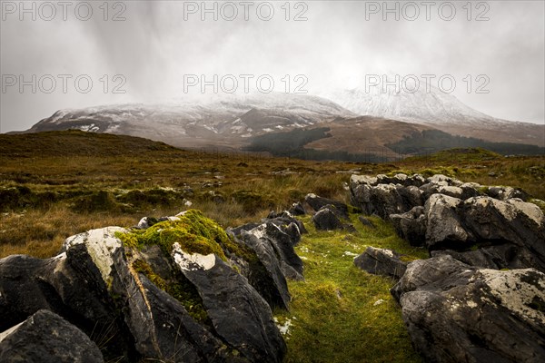 Dark rocks with white caps in Highland landscape with snow-covered Cullin mountains in the background