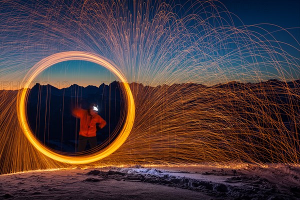Fire hoop with flying sparks on mountain peaks in front of sunrise