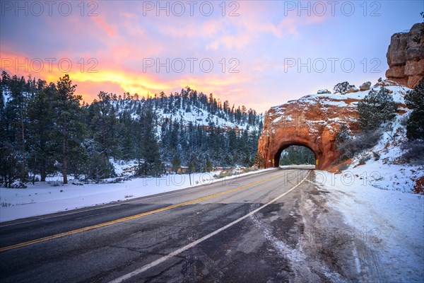 Road with tunnel through red rock arch in snow