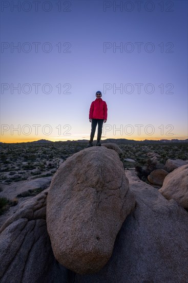 Young woman standing on round granite rocks at sunset