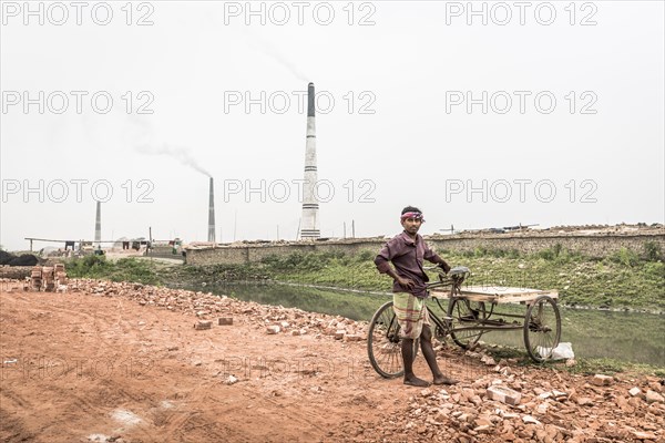 Worker with a rickshaw in front of a brickyard