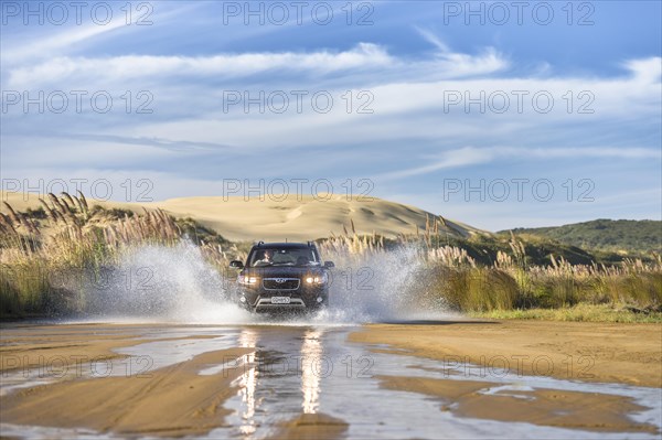 Black Hyundai Santa Fee 4x4 off-road vehicle driving through a streambed on approach to Ninety Mile Beach with sand dune behind