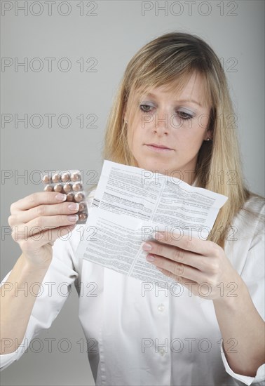 Young woman reading the package insert of a drug holding tablets in hand