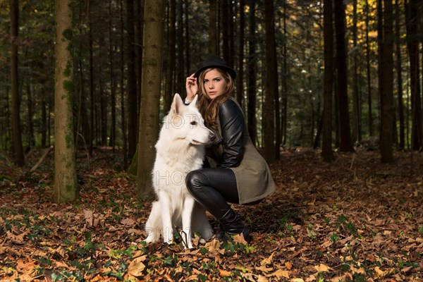 Blonde woman with white shepherd dog in the forest