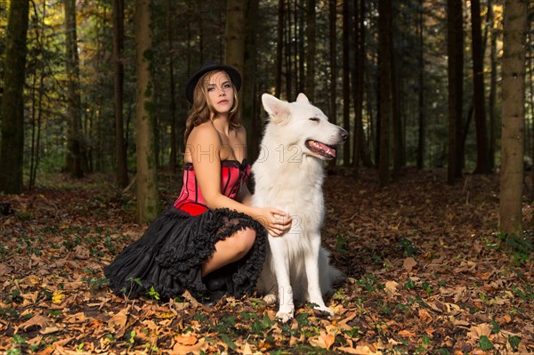 Blonde woman with white shepherd dog in the forest