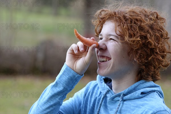 Teenager using a carrot as a long nose