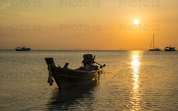 Long-tail boat in sea at sunset