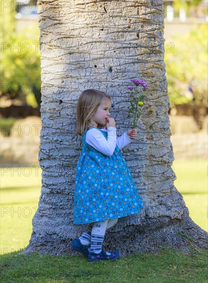 Girl with bouquet leaning against palm trunk