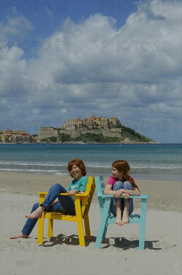 Children sitting in colorful beach chairs on the beach of Calvi