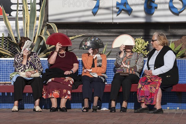 Women protecting their faces from the sun with fans