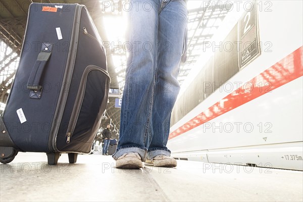 Woman in jeans and sneakers with suitcase waiting at the platform at the train station