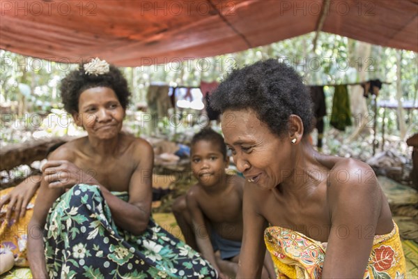 Women and children of the Orang Asil tribe sitting under tarpaulins in the jungle