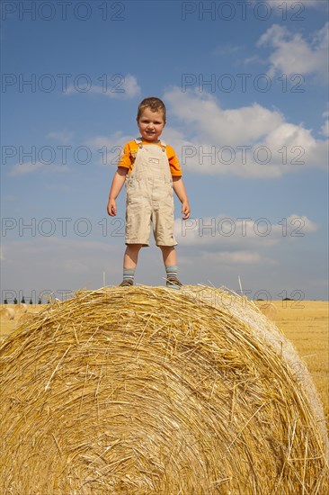 Little boy standing proudly on a straw bale