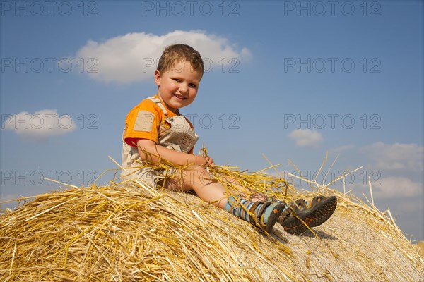 Little boy sitting on a straw bale under a cloudy blue sky