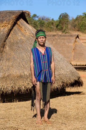 Man in traditional costume in front of a Phnong house