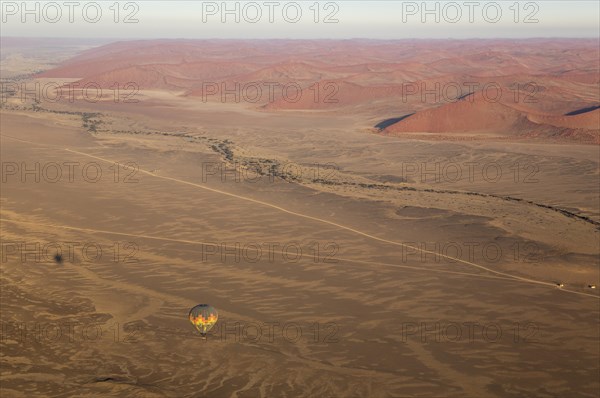 Hot-air balloon above an arid plain and the dry riverbed of the Tsauchab river at the edge of the Namib Desert