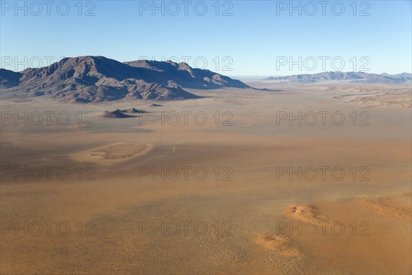 Arid desert plains with so-called Fairy Circles and isolated mountain ridges at the edge of the Namib Desert