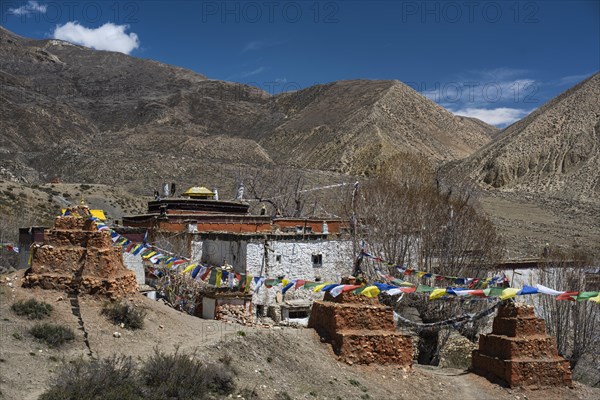 Ghar Gompa of Lo Gekar with prayer flags in front of mountain landscape